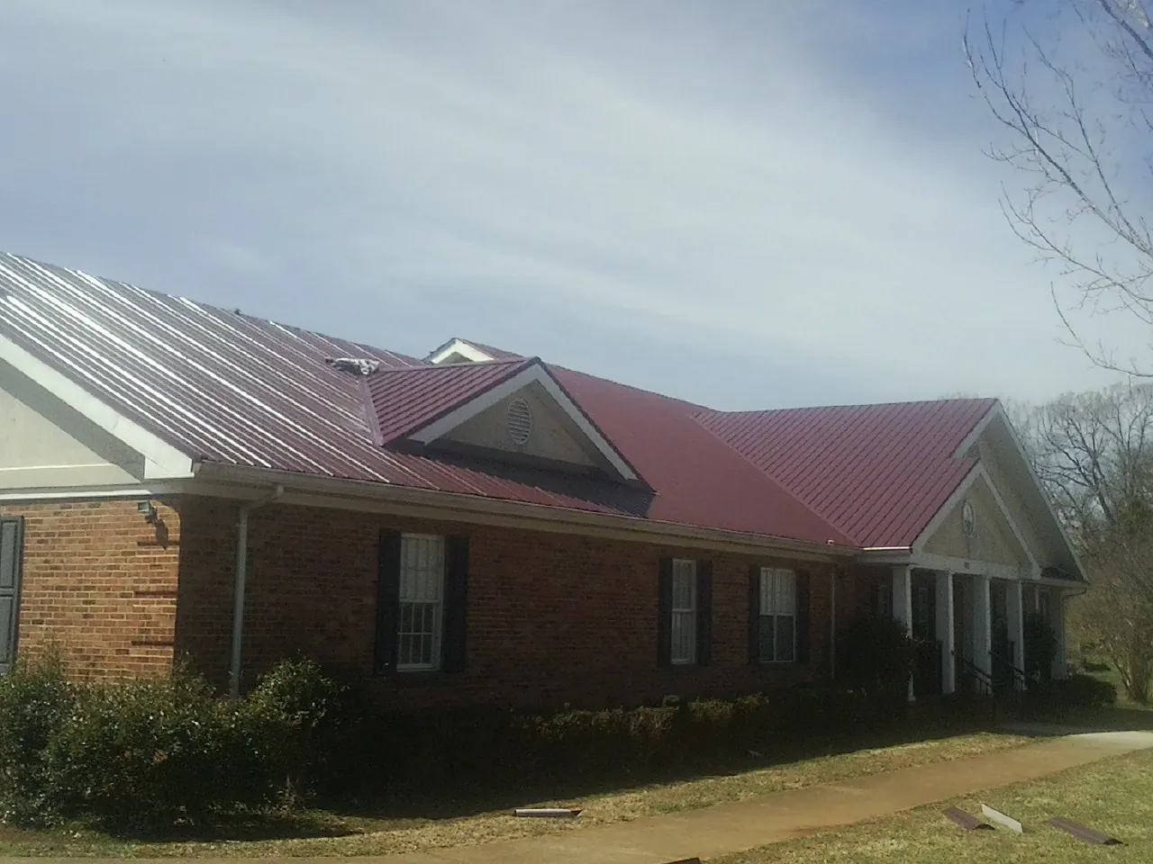 Red metal roof with gabled entries on a long brick building, from a Hail Damage Roof Repair job in Bay Saint Louis