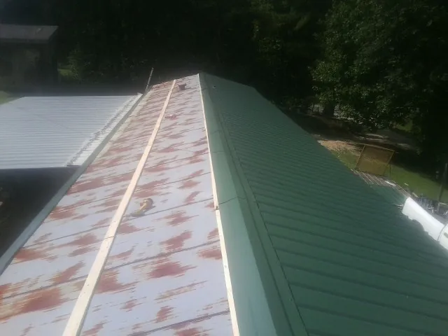 Old rusted panels beside newly installed green metal roofing — Wind Damage Roof Repair by Roofing Brothers in Bay Saint Louis