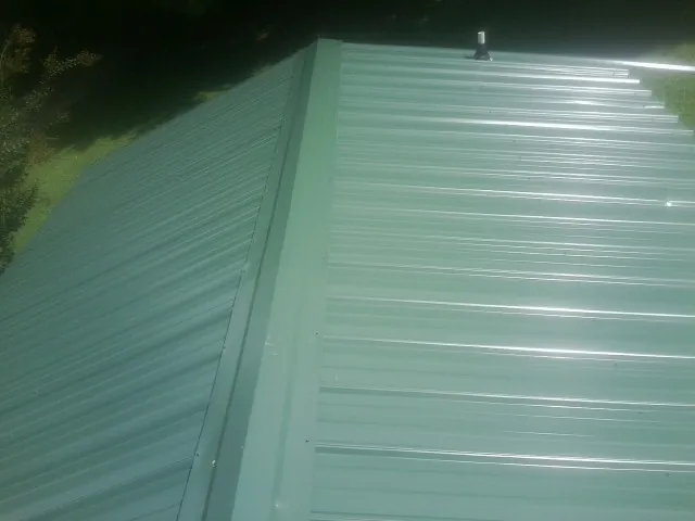 New green metal panels meeting at the ridge of a roof — Flat Roof Repair work by our crew in Bay Saint Louis