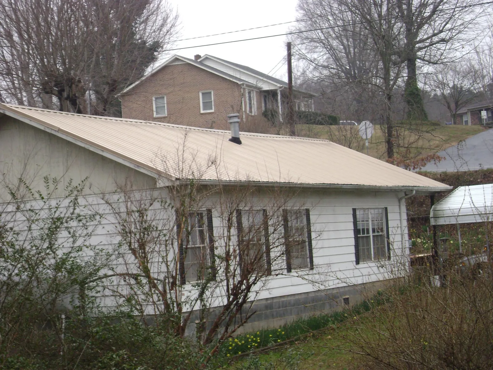 Tan metal roof on a white sided house set into a hillside — Commercial Roofing by Roofing Brothers in Bay Saint Louis