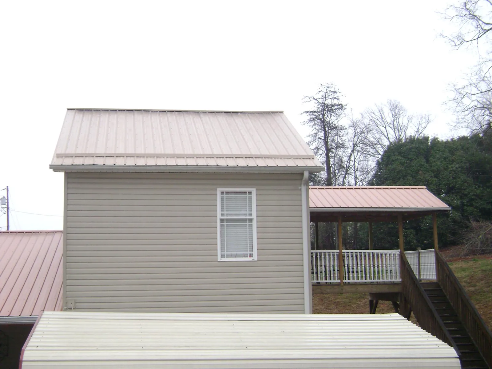 Tan metal roofs on a two story addition and attached porch, from a Roof Replacement job in Bay Saint Louis